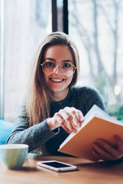 Neşeli kız öğrenci portresi. Kapalı bir yerde oturmuş ve gelecek için planlar yapıyor. Mutlu, zeki hippi kız boş zamanlarını birlikte çalışarak geçiriyor ve kameraya bakıyor.