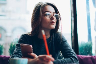 Düşünceli kadın blogcu, kampüs kafeteryasında sosyal ağ ile ilgili ilginç bir fikri olan yeni bir yazı yazmayı planlarken düşünceli bir şekilde kenara bakıyor. Kapalı alanda not defteriyle çalışan düşünceli hippi kız.