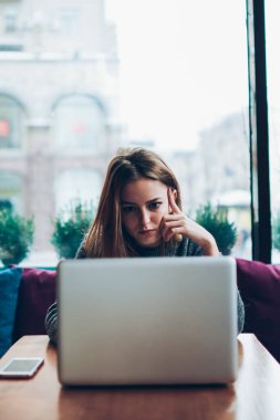 Kafeteryada dizüstü bilgisayarla otururken iş yerindeki görevler hakkında endişelenen genç, ciddi kadın yazarlar, konsantre hipster kız çevrimiçi kurs yoluyla programlamayı öğreniyor.