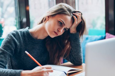 Modern dizüstü bilgisayar ve ders kitabı kullanarak yeni çizimler oluşturan yorgun kadın grafik tasarımcısı, endişeli yenilikçi kız çevrimiçi dil öğreniyor ve kapalı alanlarda yeni bir uygulama yüklüyor