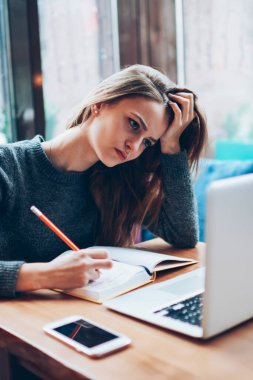 Modern dizüstü bilgisayar ve ders kitabı kullanarak yeni çizimler oluşturan yorgun kadın grafik tasarımcısı, endişeli yenilikçi kız çevrimiçi dil öğreniyor ve kapalı alanlarda yeni bir uygulama yüklüyor