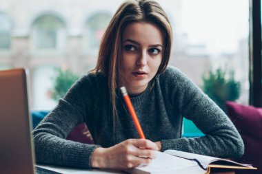 Yetenekli kadın blogcu düşünceli, sosyal ağlarda yayınlanması için bir kenara yazı yazmayı düşünceli, akıllı hippi kız ev ödevlerini ev bilgisayarı ve ders kitabı kullanarak yapıyor.