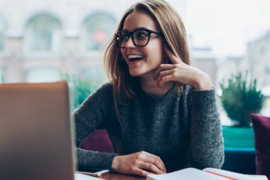 Genç mutlu bayan metin yazarı, yeni modern dizüstü bilgisayarla kafeteryada otururken yüzünde olumlu bir gülümsemeyle ev ödevini tamamlamaktan memnun kalmış tasasız bir öğrenci.