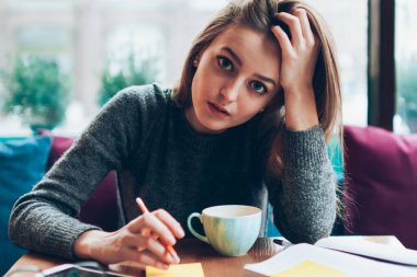 Üniversite kafeteryasında planlama için not defteriyle oturan genç ve ciddi bir kız öğrencinin portresi. Çekici hippi kız kameraya bakıyor ve ödev hazırlıyor. Çıkartmalarla notlar alıyor.