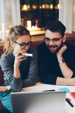 İki mutlu meslektaşın görüş koruması için gözlük. Dizüstü bilgisayar ve başlangıç projesinde çalışmaktan keyif alıyorlar. Birkaç gülümseyen hipster blogcu içeride birlikte vakit geçiriyorlar.