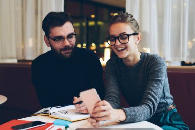 Genç hippiler sosyal ağlarda cep telefonuyla komik videolar izliyorlar üniversite kafeteryasında kablosuz bağlantıya bağlılar, akıllı telefondaki uyarıyı kontrol eden gülümseyen kız arkadaşlarıyla ders arası veriyor.