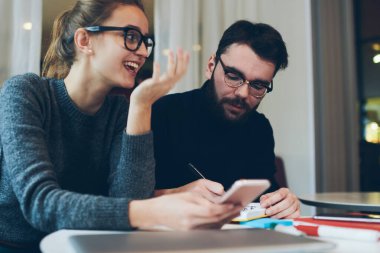 Bilgi aramak ve oteli internetten ayırtmak için not defteri ve cep telefonu kullanarak birlikte seyahat etmeyi planlayan iki pozitif öğrenci, neşeli hippi kız kafeteryada dinlenirken telefon bekliyor.