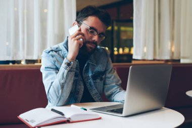Profesyonel erkek metin yazarı kafeteryada otururken uzaktan çalışmaktan zevk alıyor ve arkadaşlarıyla sohbet için akıllı telefondaki yeni uygulamayı kullanarak konuşuyor, konsantre bir adam netbook üzerinden mesaj yazıyor