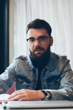 Üniversite kafe 'sinde oturan yakışıklı, ciddi bir erkek yazarın portresi. Çalışırken kameraya bakıyor. Kot giyimli modaya uygun hippi adam ve görüş düzeltici gözlük takıyor.