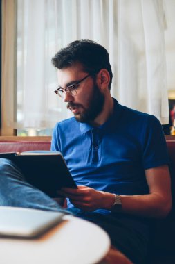 Yakışıklı sakallı hippi rahat giyinmiş edebiyattan zevk alan rahat kafeteryada koç üzerinde dinlenen genç, moda odaklı erkek öğrenci boş zamanlarında ilginç hikayeler okuyor.