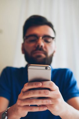 Akıllı telefona seçici odaklanma, sosyal ağlarda arkadaşlarıyla sohbet eden ve üniversite kafeteryasında arkadaşını beklerken modern cep telefonuyla 4G bağlantısı olan postaları kontrol eden yetenekli hippi çocuk.