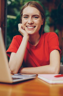 Dizüstü bilgisayarla oturup kampüs kafesinde kameraya bakan gülümseyen profesyonel kadın serbest yazar portresi, netbook ile öğrenen neşeli hippi kız ev ödevi yapıyor.