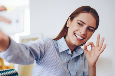Neşeli, modaya uygun hippi kız arkadaşıyla video görüşmesi yaparken modern akıllı telefondan 4G bağlantısı olan mutlu kadın kapalı mekanda fotoğraf çekmek için cep telefonu kullanıyor.