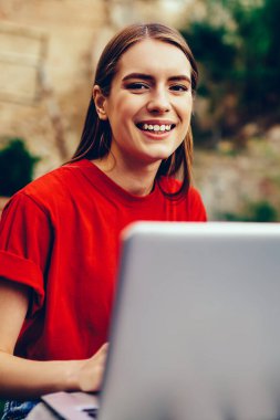 Dizüstü bilgisayarla çalışan neşeli kadın metin yazarının portresi ve açık havada gülümseyen kameraya bakmak, üniversite kampüsünde netbook üzerinden dil öğrenen neşeli hippi kız.