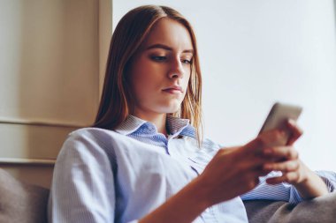 Moda kıyafetli düşünceli hippi kız işten sonra rahat koltukta elinde cep telefonuyla dinleniyor. Çağdaş akıllı telefonuyla internetten 4G internetli bir otel ayarlıyor.