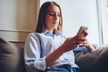 Moda kıyafetli düşünceli hippi kız işten sonra rahat koltukta elinde cep telefonuyla dinleniyor. Çağdaş akıllı telefonuyla internetten 4G internetli bir otel ayarlıyor.