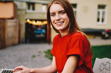 Neşe dolu pozitif kadın kullanıcının portresi sokak kafesinde oturup ileri netbook üzerinden çalışırken gülümseyen ve dışarıdaki kameralara bakan modern bilgisayar masanda duruyor.