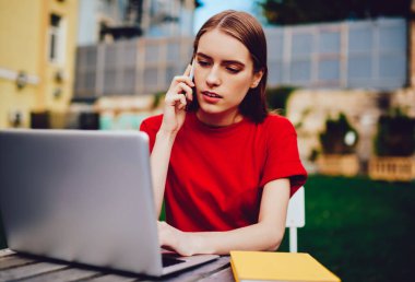 Uzaktan çalışmaktan keyif alan konsantre profesyonel metin yazarı netbook üzerinden gezinen, düşünceli kadın klavye mesajında sohbet için akıllı telefondaki yeni uygulamayı kullanarak arkadaşınla konuşuyor.