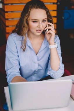 Konsantre kadın serbest çalışan, operatörle ciddi telefon görüşmeleri yaparken, uzaktaki iş için zaman ayırıyor ve kapalı alanda ücretsiz kablosuz internet kullanıyor.