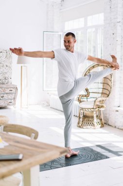 Çıplak ayaklı güçlü erkek spor giyimli. Ayaktan ayak yogası pozu üzerinde çalışırken dengede duruyor.