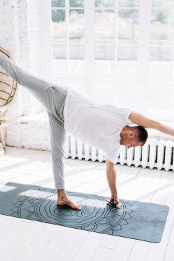 Yüksek açılı çıplak ayaklı erkek, çıplak ayaklı, odada yoga yaparken Half Moon pozu veriyor.