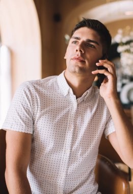 Gündüz vakti bar tezgahının yanındaki kafede kokteyl içerken akıllı telefondan konuşan, gündelik kıyafetli, kendine güvenen bir adam.