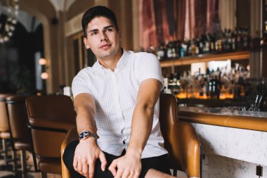 Rahat genç erkek rahat kıyafetler ve spor ayakkabılar içinde şık bir kafede bacak bacak bacak üstüne atmış bir şekilde otururken başka tarafa bakıyor.