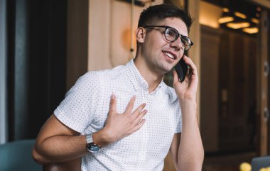 Bilgisayarlı genç bir serbest çalışan cep telefonuyla konuşuyor ve kafede oturmuş hayal kurarak yüzünü çeviriyor.