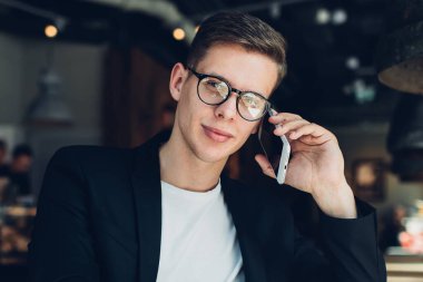 Kendine güveni tam bir adam, modern bir restoranın masasında oturmuş, iş projesinde not defterine planlar yazıyor ve cep telefonuyla konuşuyor.