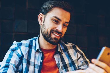 Neşeli sakallı genç adam komik Haberler Blog için 4 g bağlı smartphone aygıt üzerinde okuma rahat kıyafet giymiş Internet. Pozitif hipster adam modern cep telefonu online video izliyor