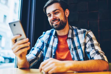 Başarılı sakallı modern smartphone cep telefonu ile 4 g üzerinden online sohbet mesajlaşma delikanlı uzay coworking oturan internet. Pozitif hipster blogger ile hücresel cihaz üzerinde iyi haber bildirim okuma