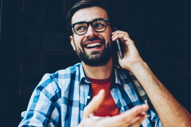 Olumlu erkek smartphone üzerinde arama ve telefon görüşmesi sırasında arkadaşlarınızla konuşurken blogger sakallı. Casual giyim hücresel coworking içinde oturan iletişim kurulurken gülüyor neşeli genç adam
