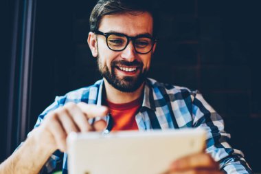 Modern tablet tarihinde yayına izlerken gözlük olumlu sakallı hippi adam bağlı 4 g için Internet. Casual kıyafet online dijital dokunmatik ped cihaz üzerinde sohbet içinde neşeli erkek blogger