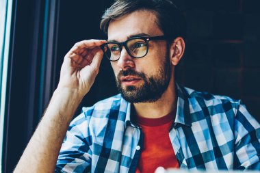 Uzağa bakıyor ve kendi blog geliştirmek için fikirleri üzerinde düşünme dokunmatik yüzey ile düşünceli sakallı genç adam. Gözlük vizyon düzeltme modern tablet elinde tutan durulması hipster adam