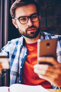 Aramak için gözlük kartvizit elinde tutan ve akıllı telefon numarası çevirmeden vizyon düzeltme için genç adam sakallı. Dalgın yakışıklı erkek blogger telefon hakkında bilgi arama