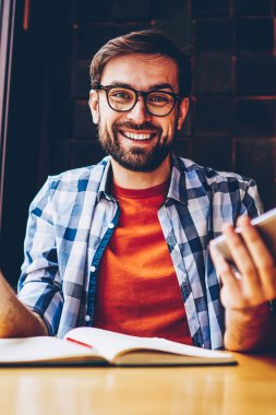 Mutlu sakallı genç adamın yarım uzunluk portre rahat kıyafet ise kredi kartı tutan ve smartphone aygıt üzerinde 4 g internet bağlantısı üzerinden para işlem yapma kameraya gülümseyen giyinmiş