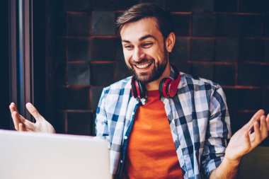 Mutlu sakallı hippi blogger modern dizüstü bilgisayarda görüntülü görüşme yoluyla arkadaşlarınızla iletişim kurmak için kablosuz 4 g bağlı internet. Komik eğitsel bir netbook izlerken boyun kulaklık ile pozitif genç adam