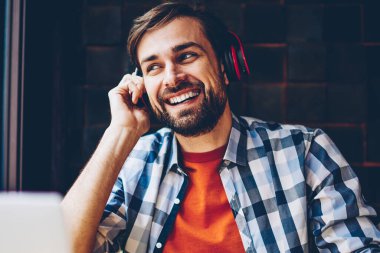 Telefon için Bluetooth kulaklık elektronik müzik zevk olumlu sakallı blogger bağlı. Neşeli rahat giyinmiş genç adam dinleme ses şarkı çalma listesinden Smartphone'da indirilen