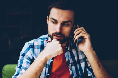 Coworking içinde oturan Smartphone cep telefonu ile telefon görüşmesi sırasında operatör ve değişim tarife planı hakkında düşünme dinleme telefon önerisi düşünceli sakallı genç adam. Sakallı hippi adam cep üzerinde bahsediyoruz