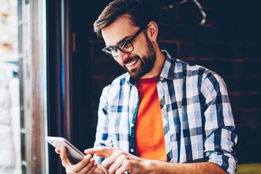 Neşeli sakallı blogger smartphone aygıt üzerindeki sosyal ağlar komik yorum okuma için 4 g bağlıyken gülüyor Internet. Modern cep üzerinde arkadaşlarınızla sohbet online olumlu hippi herif