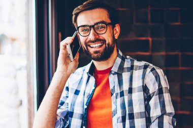 Mutlu sakallı genç adam portresi smartphone telefon görüşmesi sırasında ilgili komik Haberler arkadaşıyla konuşurken kameraya gülümseyen trendy forması giymiş. Neşeli hipster adam cep üzerinde iletişim