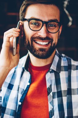 Yarım uzunlukta gözlük Smartphone'da çağrılırken kameraya gülümseyen vizyon düzeltme başarılı genç adam portresi. Pozitif hipster adam işleç ile ATT yararları hakkında Evet