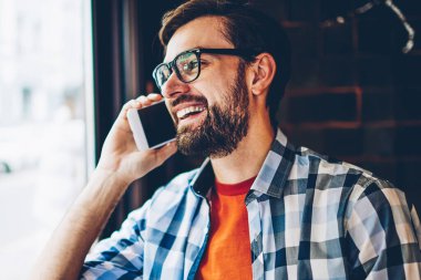 Mutlu sakallı hippi adam gözlük sırasında telefon konuşma bir arkadaşım Smartphone cep telefonu ile gülüyor. Gülümseyen ve dijital cep telefonu üzerinde konuşurken rahat şık gömlek giymiş olumlu genç adam