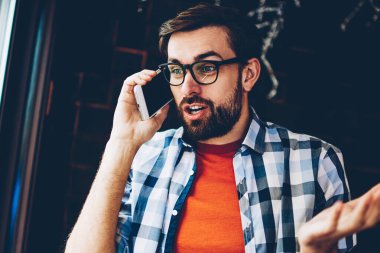 Sakallı genç adam şaşırmış arkadaşı ile telefon görüşmesi sırasında dijital smartphone aygıt üzerinde konuşuyor haberleri ile hayran. Hipster adam heyecan şok hikaye modern telefonla arama ile merak ettim