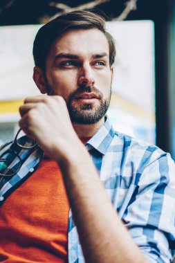 Optik gözlük pencereden dışarı bakıyor ve kendi başlangıç projesi geliştirmek için yaratıcı fikirler üzerinde düşünme sırasında elinde tutan rüya gibi yakışıklı genç adam. Düşünceli hipster adam planları üzerinde durulması