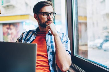 Düşünceli sakallı grafik tasarımcı düşünme üzerinde Web sitesi geliştirme ve modern dizüstü cihaz alan coworking içinde ücretsiz 4 g internet bağlantısı kullanarak, serbest çalışma pencereden dışarı seyir için fikirler
