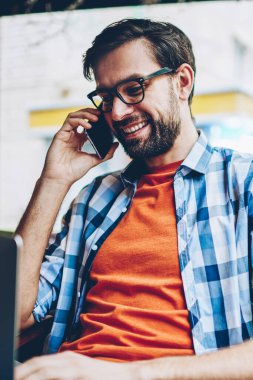 Happy sakallı genç adam gözlük smartphone yazılım yolu ile radyo 4 g modern dizüstü bilgisayarda güncelleştirilirken iletişim internet. Netbook hücresel oturma konuşurken olumlu hipster adam