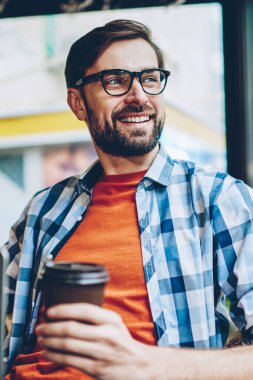 Gülümseyen hayal pencereden dışarı bakıyor ve öğle arasında Web sitesi geliştirmek için yaratıcı fikirler üzerinde düşünme genç adam sakallı. Düşünceli neşeli erkek blogger ile netbook aygıt çalışma gitmek için kahve