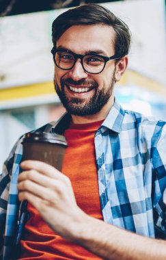Yarım uzunluk portre mutlu yakışıklı el ve kameraya gülümseyen gitmek için kahve tutan gözlük öğrenci sakallı. Uzay coworking dinlenme içecekler ile olumlu erkek blogger