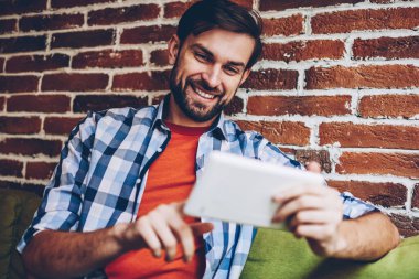 Mutlu sakallı genç adam modern Dokunmatik ped cihaz üzerinde Web sitesinde komik Haberler okuma rahat gömlek giymiş. Neşeli hipster blogger yayın 4 g internet bağlantısı üzerinden dijital tablet İndiriyor